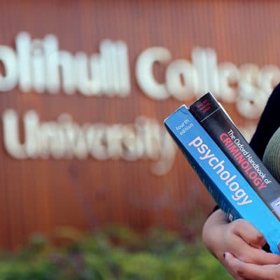 Girl stands holding books in front of college.