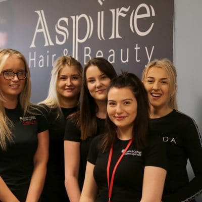 Hair & beauty students stood in front of Aspire sign