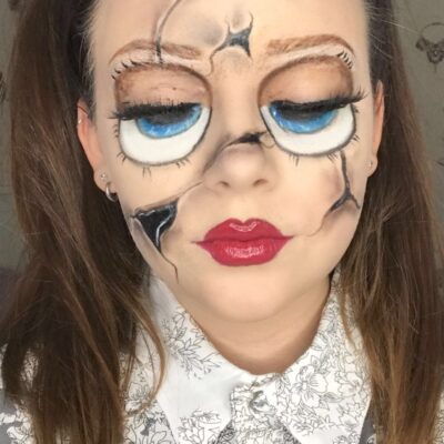 a student has painted herself as a cracked china doll with cracks down her face