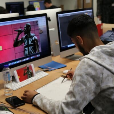 a student designs a poster on his computer and sketches the design on paper before the mac at his desk