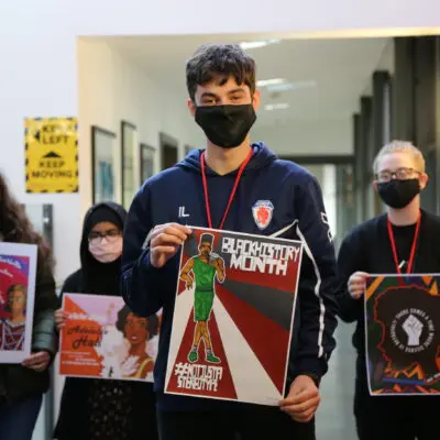 a young man stands in front of his fellow students holding their poster efforts