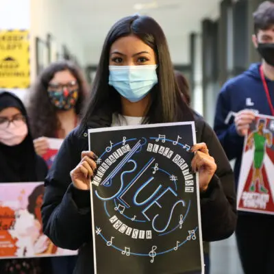 5 students hold up their poster efforts for the competition, all wear masks
