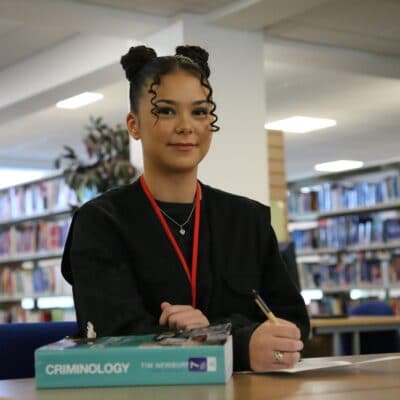 Nicole working in the library with a criminology textbook at her side on the desk
