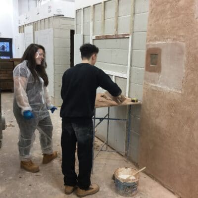 Rachel Arnold discusses the project in front of a plastering wall with a student.