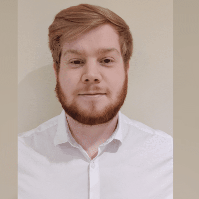 Sam Teal stands in a white shirt smiling portrait style at the camera.