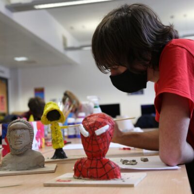 A male student paints a yellow hooded clay character.