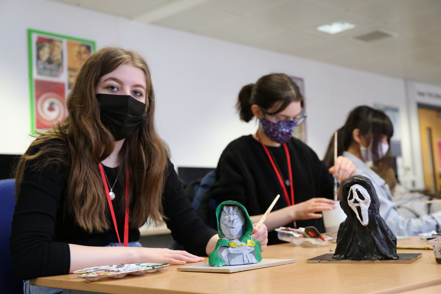 Student Jenna sat in a classroom painting her model on the desk with others sat behind her.