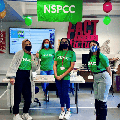 three students and an LSA stand in front of an NSPCC Banner in charity tshirts.