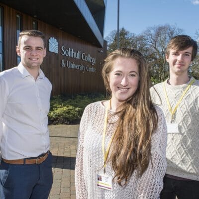 one female apprentice and two male apprentice stand outside the blossomfield campus entrance smiling
