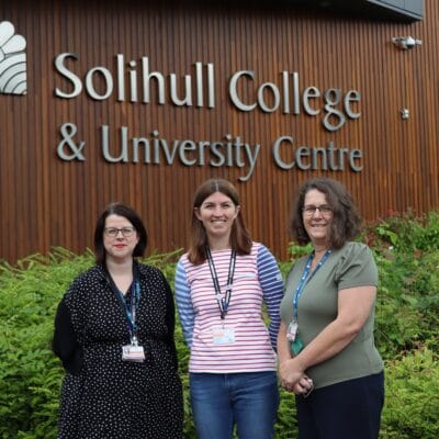 Kerry Scattergood with contributors Isla Flood and Carol Baker stood outside the College with the sign behind them