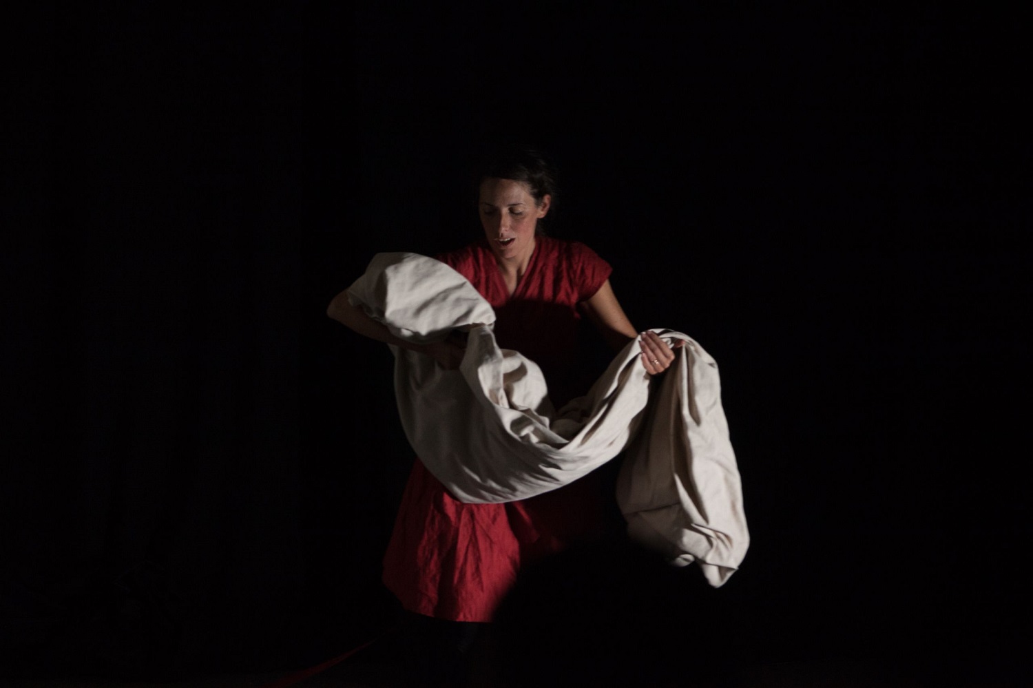 Joanne in a play stood against a black background carrying a sheet in her arms.