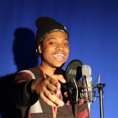Remar stands in front of a mic in a media studies studio