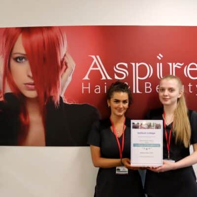 Two students hold certificate in front of banner entitled Aspire Hair & Beauty