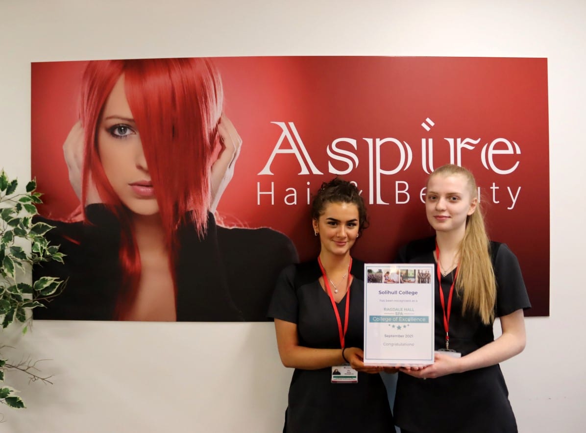Two students hold certificate in front of banner entitled Aspire Hair & Beauty