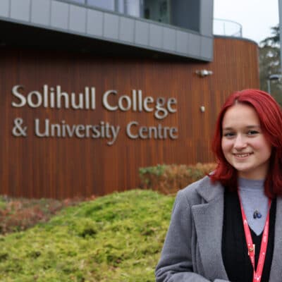 Student standing in front of building with sign behind her that reads Solihull College & University Centre