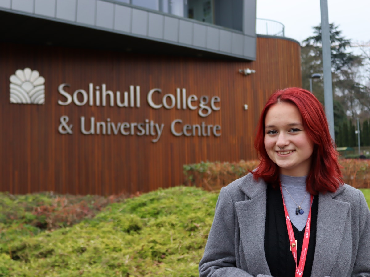 Student standing in front of building with sign behind her that reads Solihull College & University Centre
