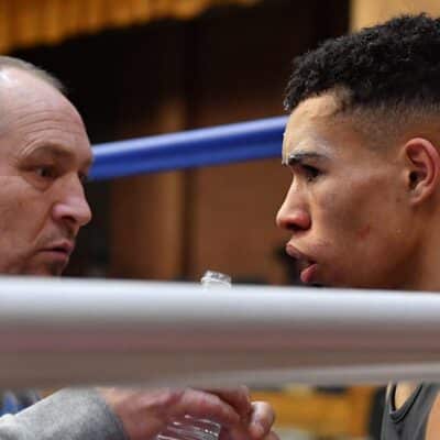 two men in corner of boxing ring zoomed into face coach is cleaning boxer's face