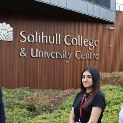 Councillor and two students standing in front of campus building