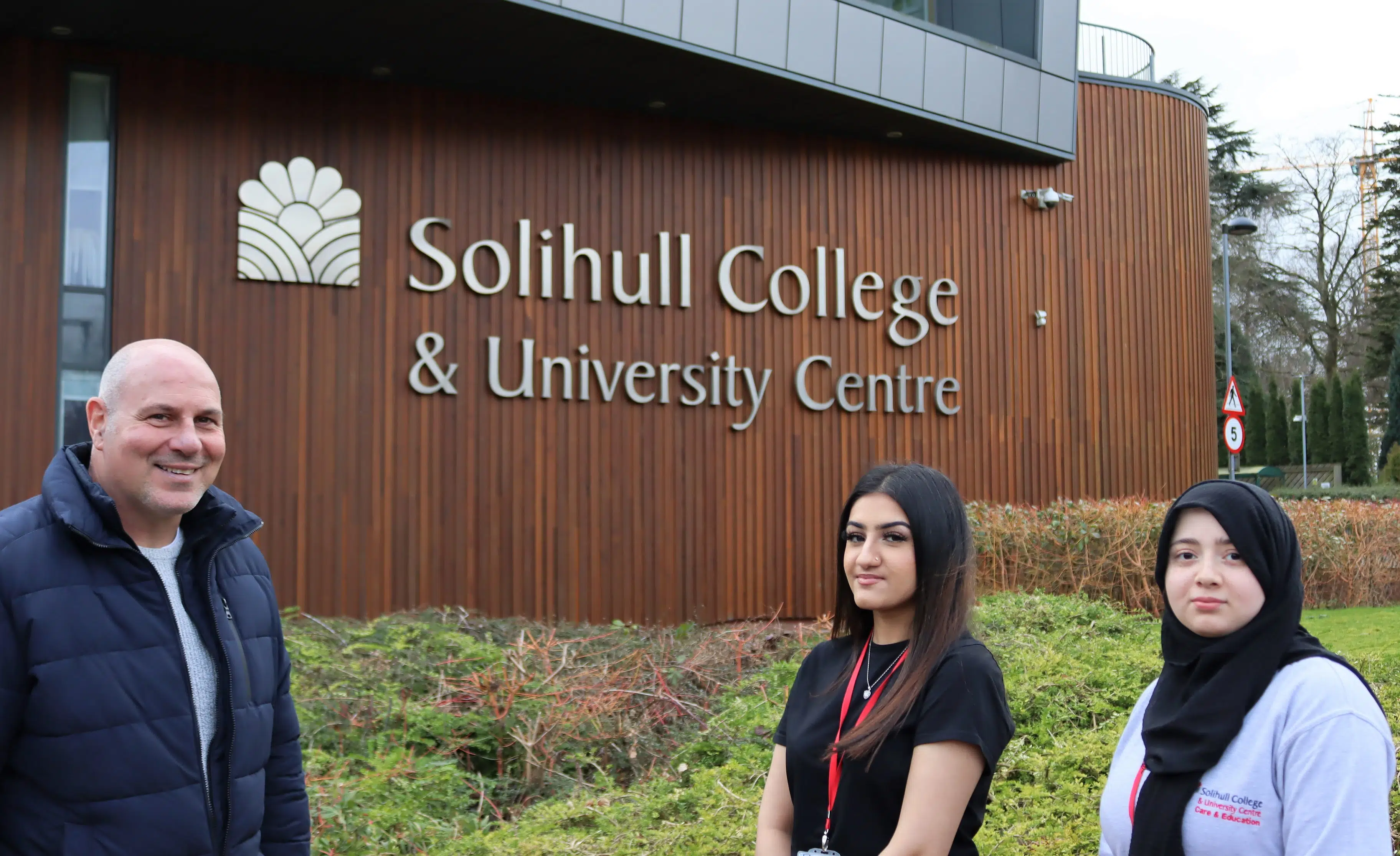 Councillor and two students standing in front of campus building