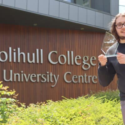 Student holding award in front of college