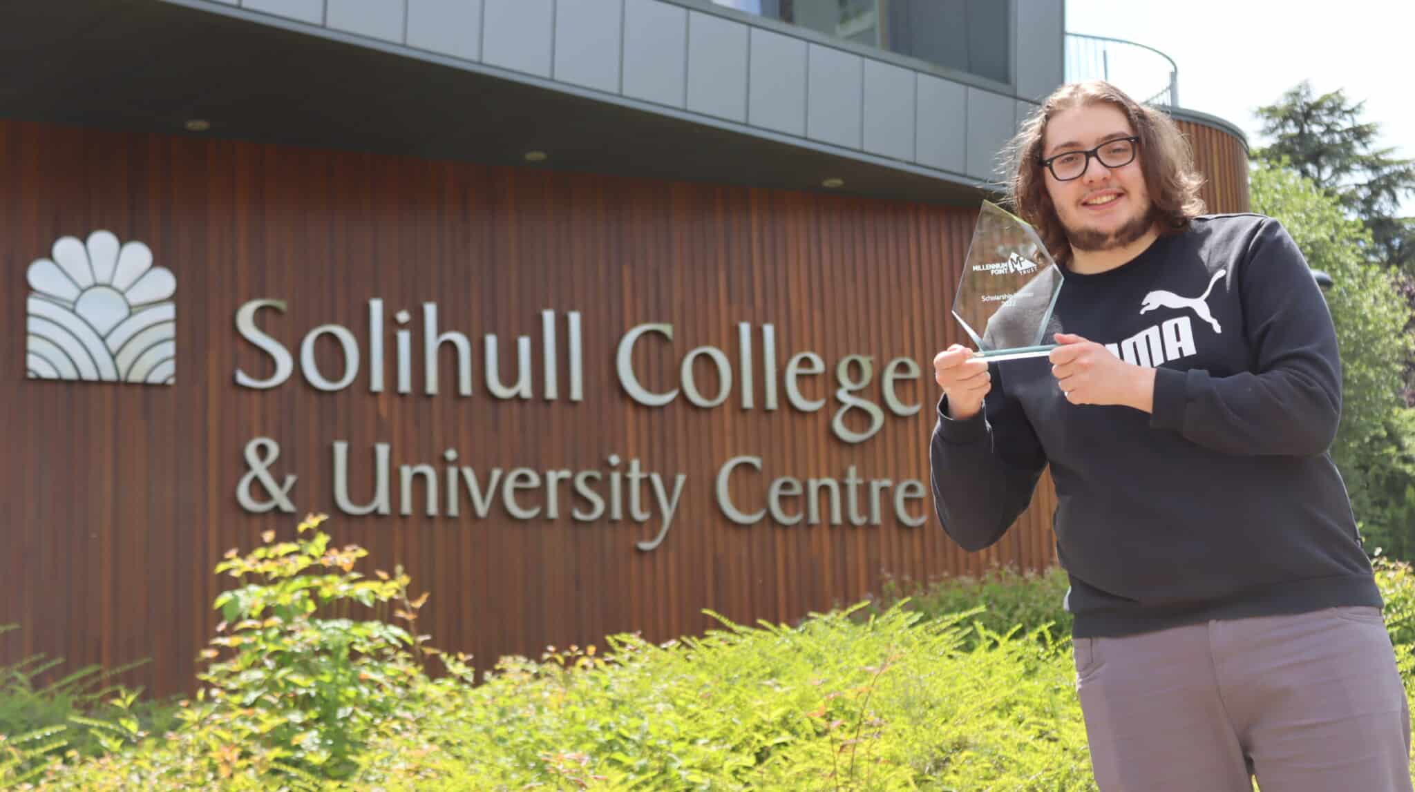 Student holding award in front of college