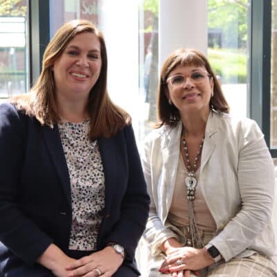 Rebecca and Mary sitting in front of glass window smiling at camera