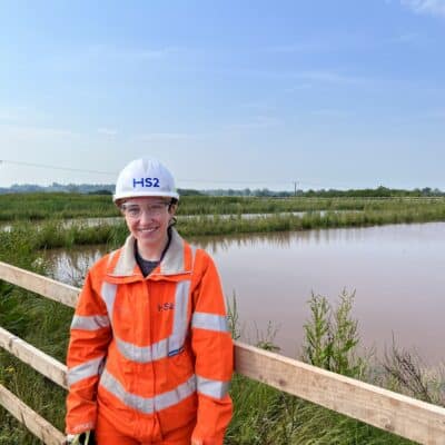 Alice wearing orange hi vis jacket and hard hat at HS2 site