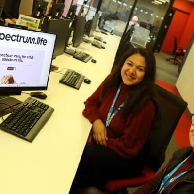 two Solihull College staff members looking up at camera sat next to computer screen