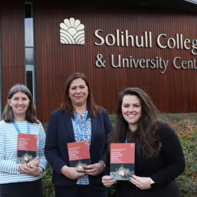 3 staff member holding book in front of college