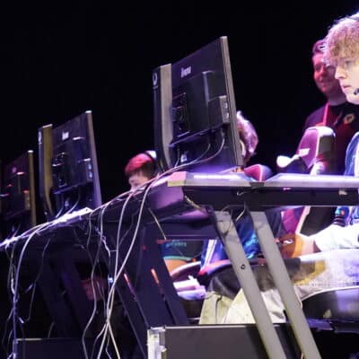 Students sat an a computer with headphones on playing on it