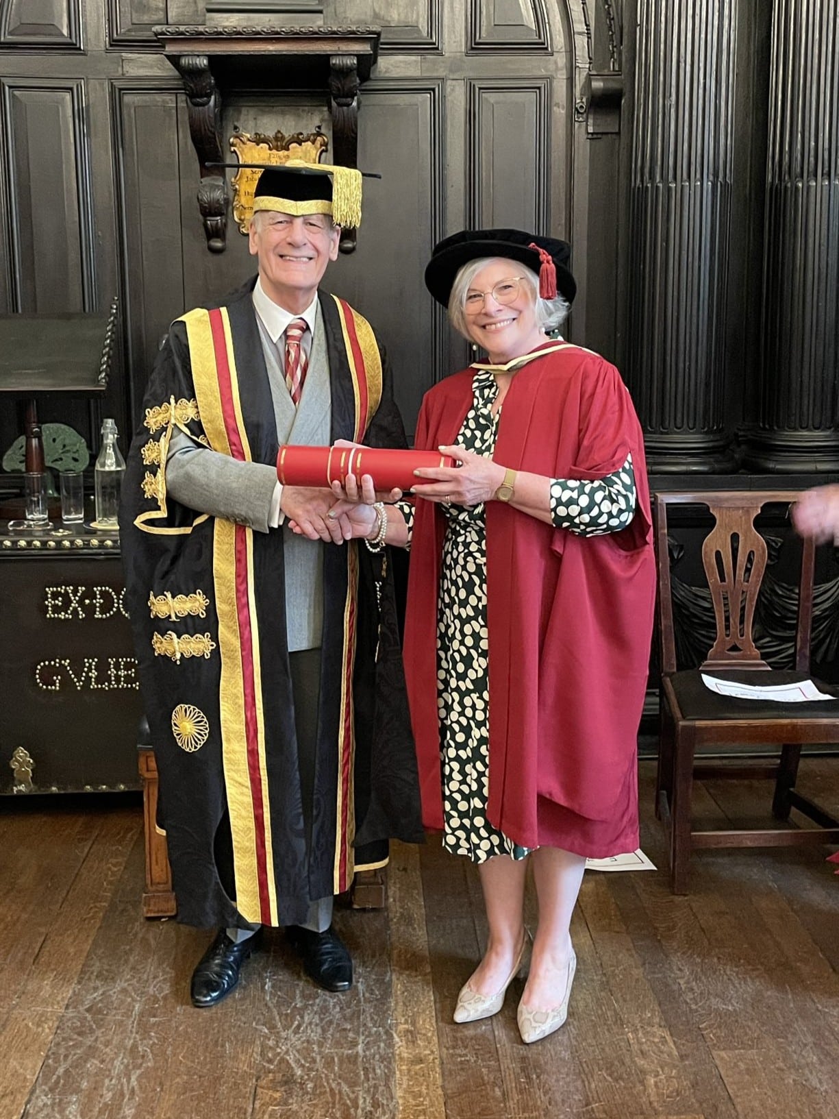 A man with a robe and a hat, and a woman in a red robe receiving an award.