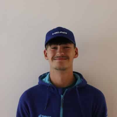 A boy in a hat stood on a white wall smiling