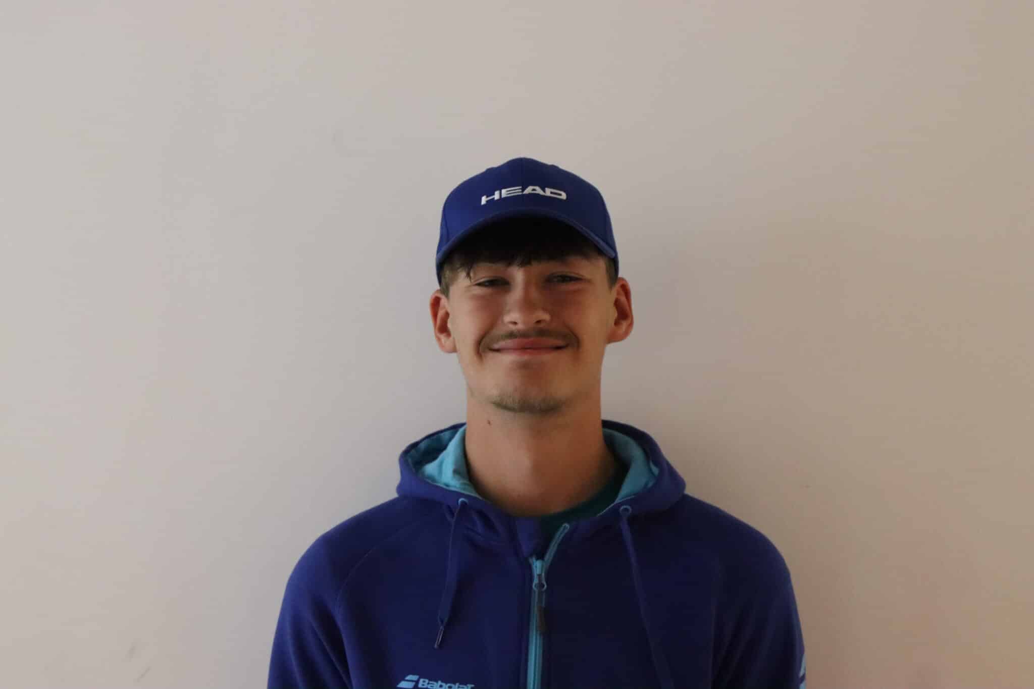 A boy in a hat stood on a white wall smiling