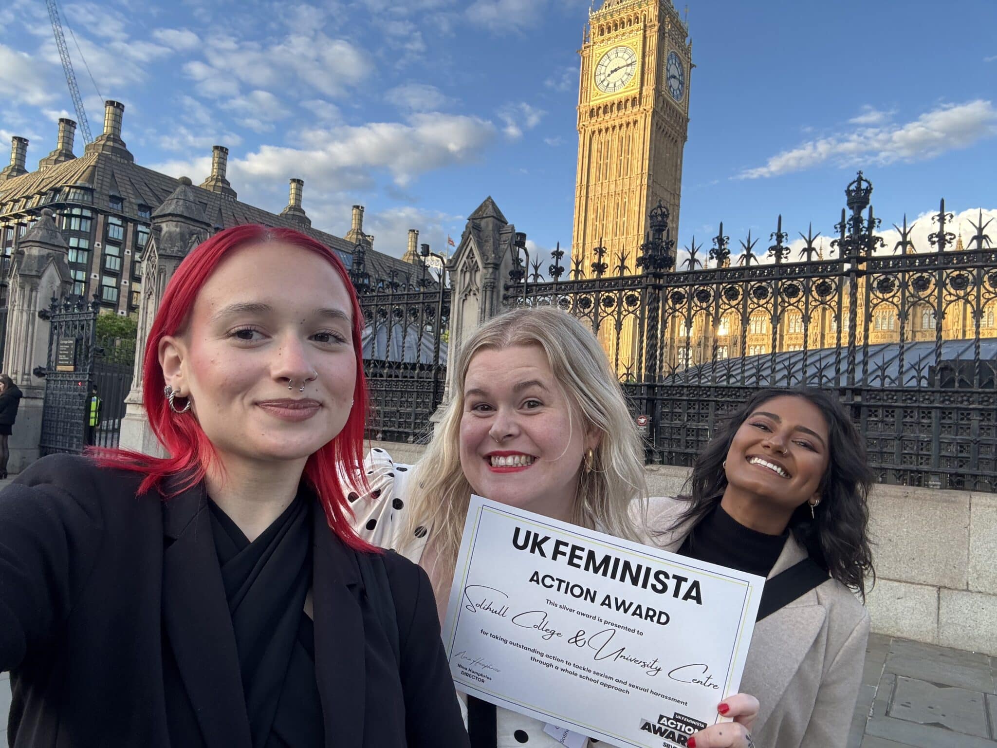 3 adult women stood outside parliament with Big Ben in the background.